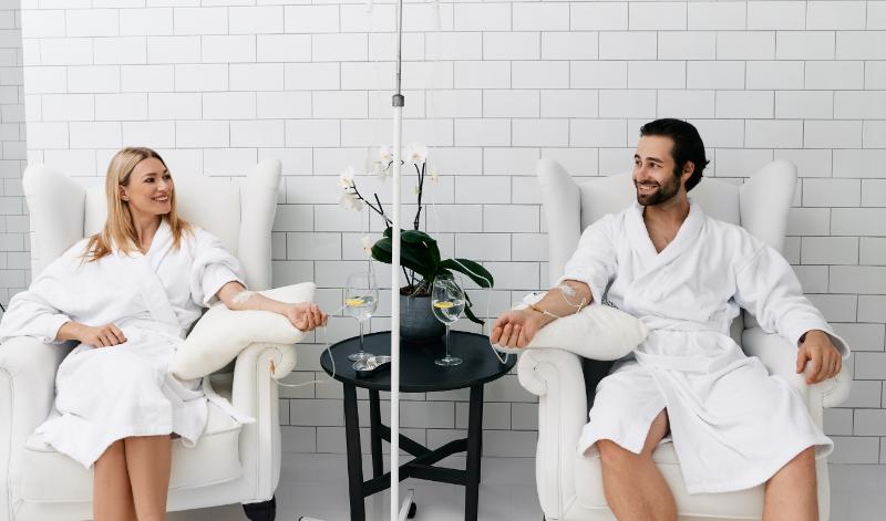 Two individuals receiving IV therapy in a relaxing clinic setting.